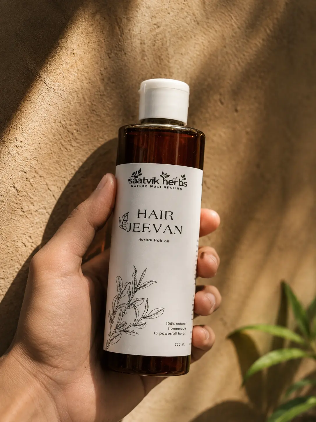 A hand holding the Hair Jeevan bottle against a sunlit wall, with a plant in the corner of the frame